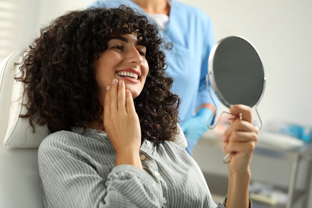 Woman in dental chair smiling at reflection in handheld mirror